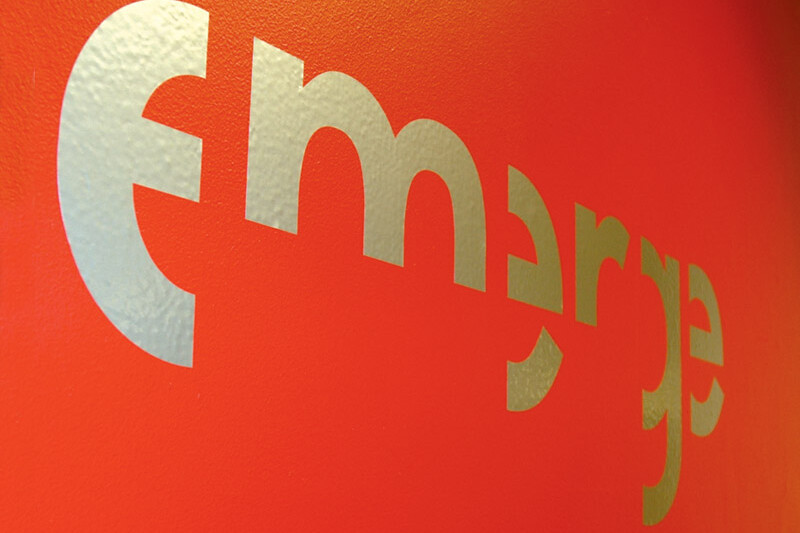 Photograph of Emerge logo on red wall